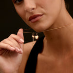 Close-up of a woman wearing a delicate gold necklace with heart and key pendant against a dark background