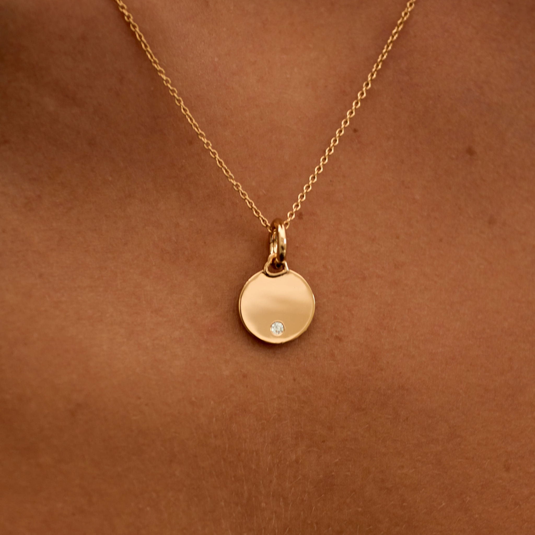 Gold necklace with a round pendant on a person's neck against a brown background