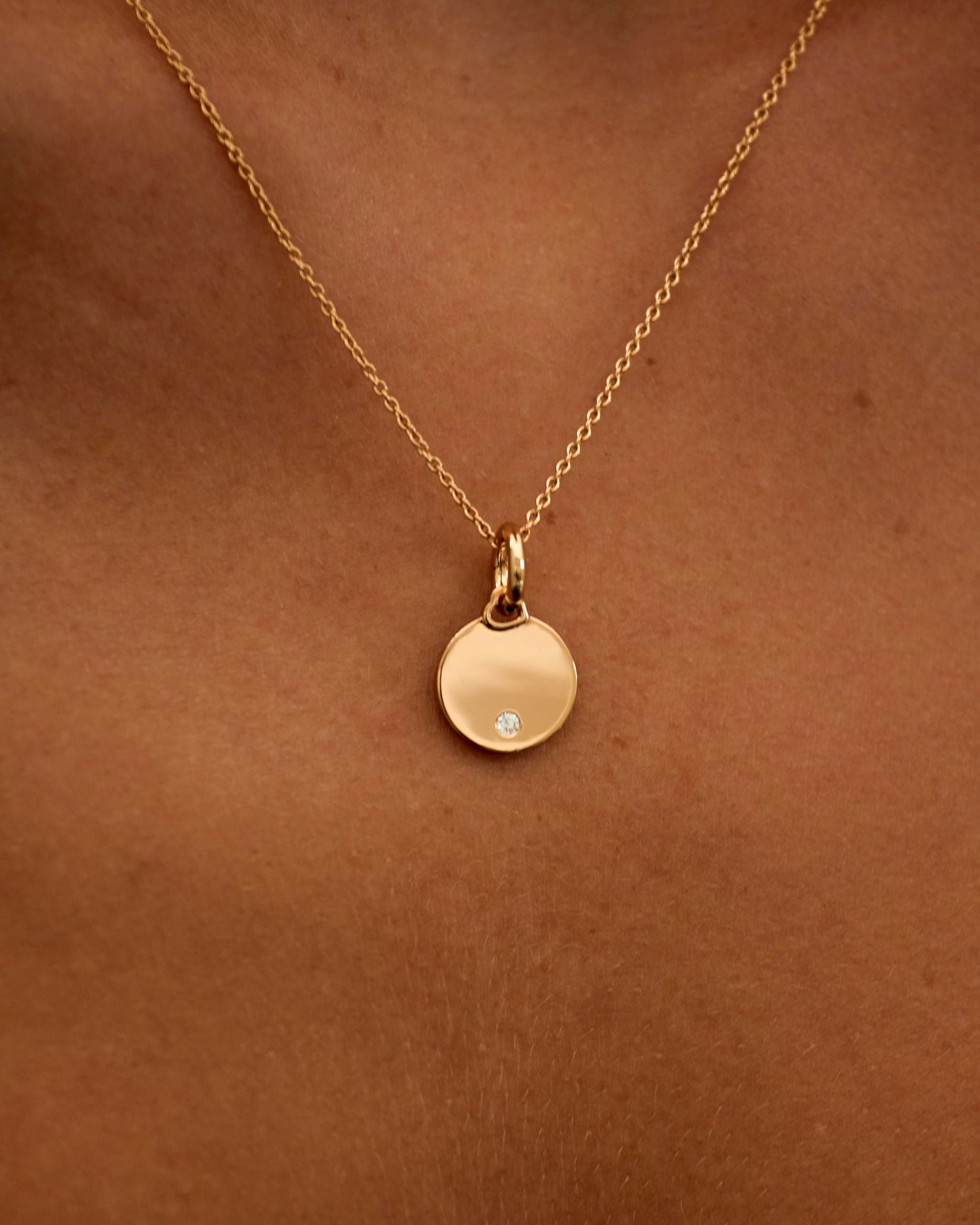 Gold necklace with a round pendant on a person's neck against a brown background