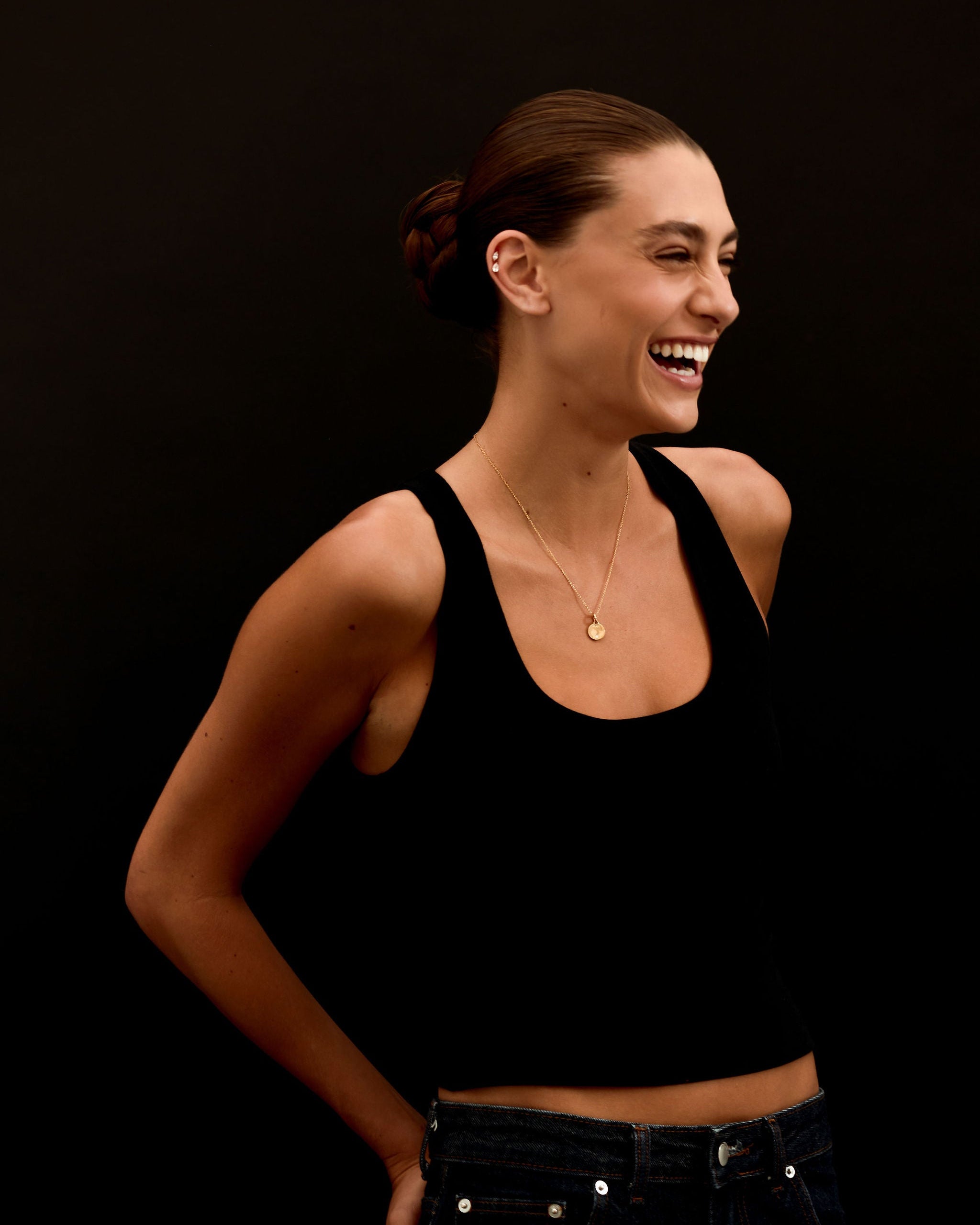 Woman wearing a black tank top and jeans against a black background