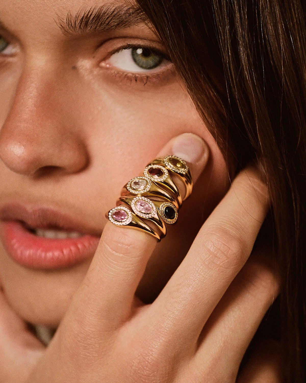A close-up lifestyle shot of a model wearing a gold ring with multiple stacked oval gemstone settings on her finger.